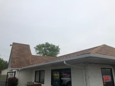 White commercial building with brick chimney, dark windows, and neon open signs against overcast sky