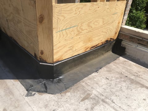 Wooden plywood wall structure with dark membrane flashing meeting concrete roof surface