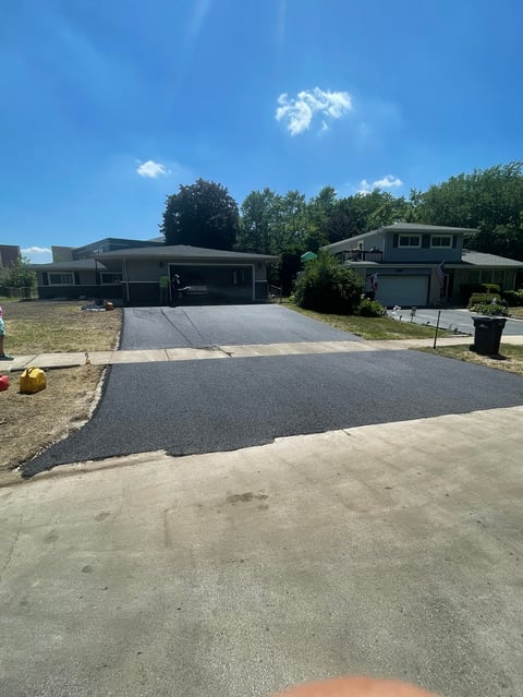 Two mid-century modern homes with newly paved asphalt driveway under clear blue sky with green trees in background