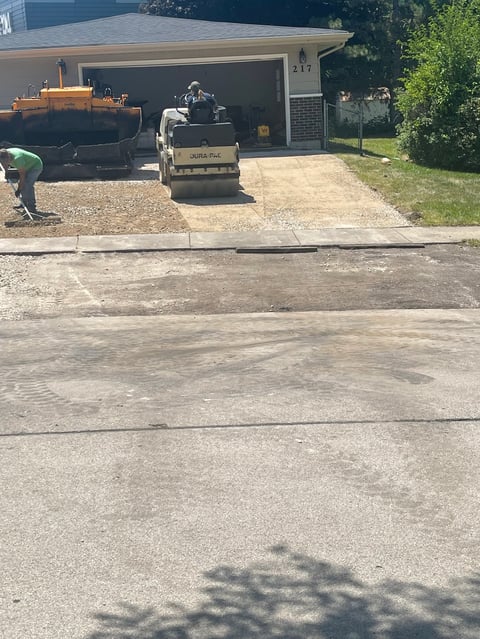Asphalt paving truck at residential driveway with workers during driveway resurfacing project