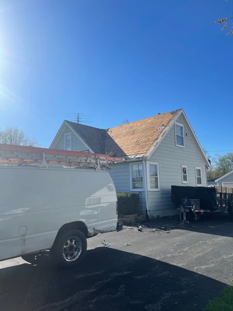 White house with partial roof replacement under construction, white van parked in driveway on clear day