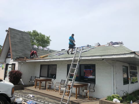 Roofers working on replacing shingles on a residential house roof with ladders and equipment visible