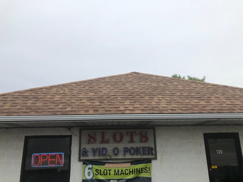 Exterior of a slots and video poker establishment with an OPEN sign and slot machines advertisement on the storefront